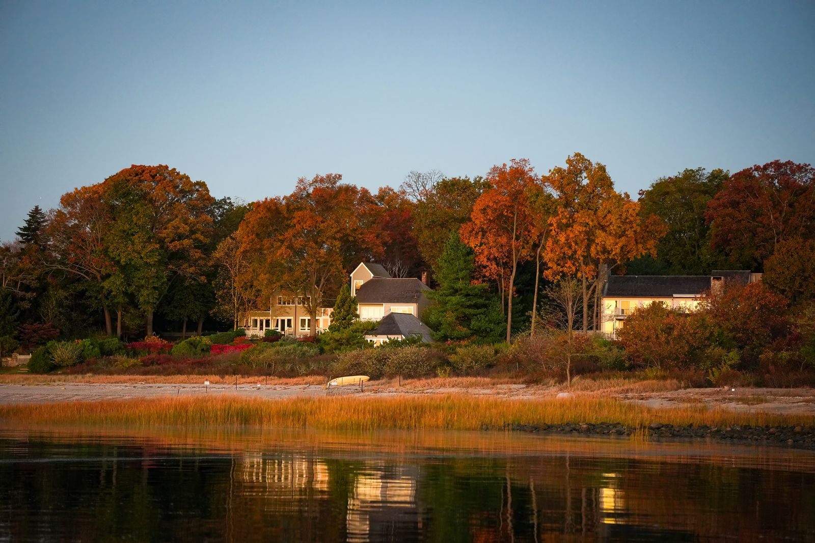 Waterfront homes framed by autumn foliage on the New England shore, the scenery of fall foliage cruises